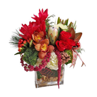 Interspersed throughout the arrangement are Christmas ornaments, shimmering in shades of gold, silver, or red, offering a festive sparkle. Flowing ribbons in complementary holiday colors—such as deep red, gold, or green—gracefully weave through the flowers, tying the entire design together. This centerpiece is a perfect blend of tropical elegance and Christmas cheer, creating a striking, celebratory statement for the holidays.